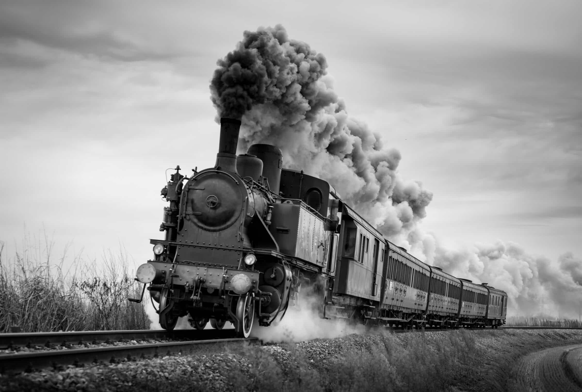 Steam train runs on the tracks on a cloudy day. Black and white photography.