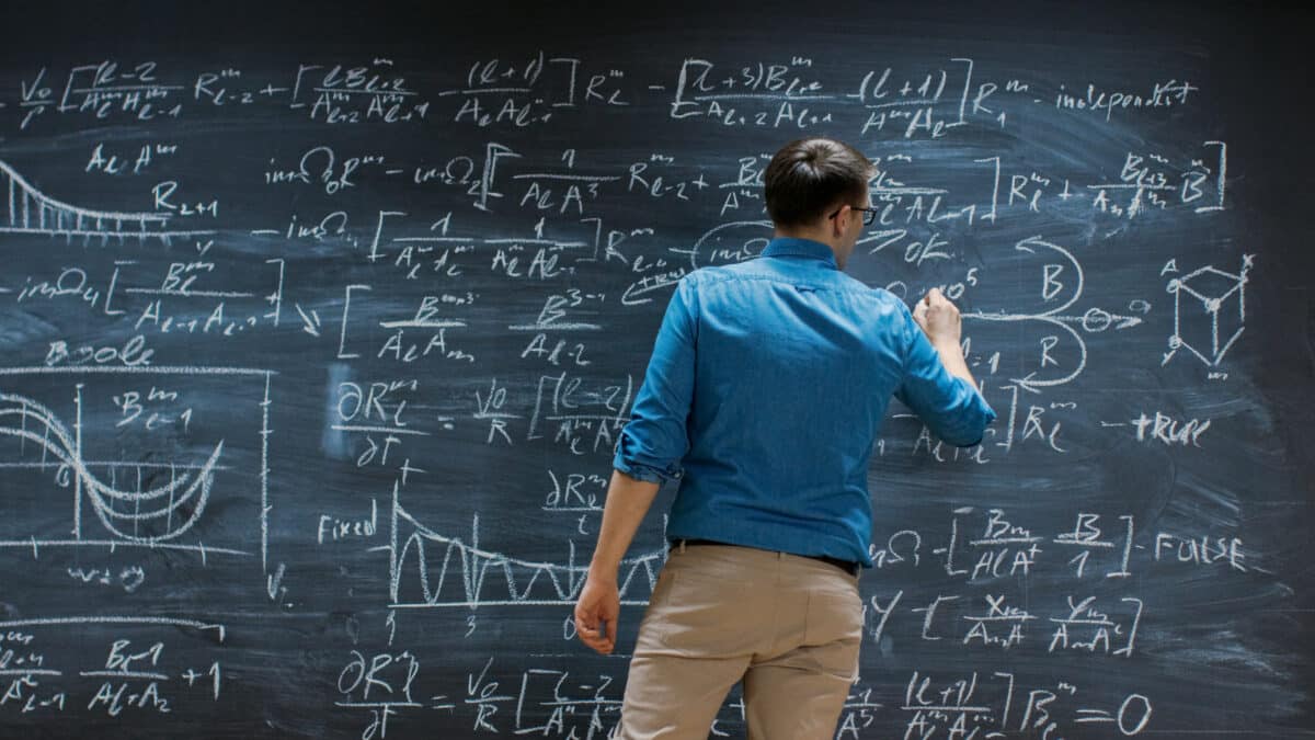 Brilliant Young Mathematician Is Writing on Big Blackboard and Thinking about Solving Long and Complex Equation/ Formula.