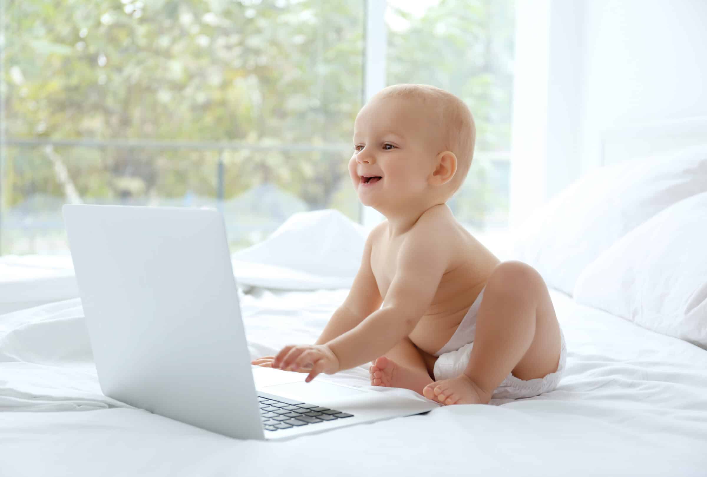 Cute baby boy with laptop on bed