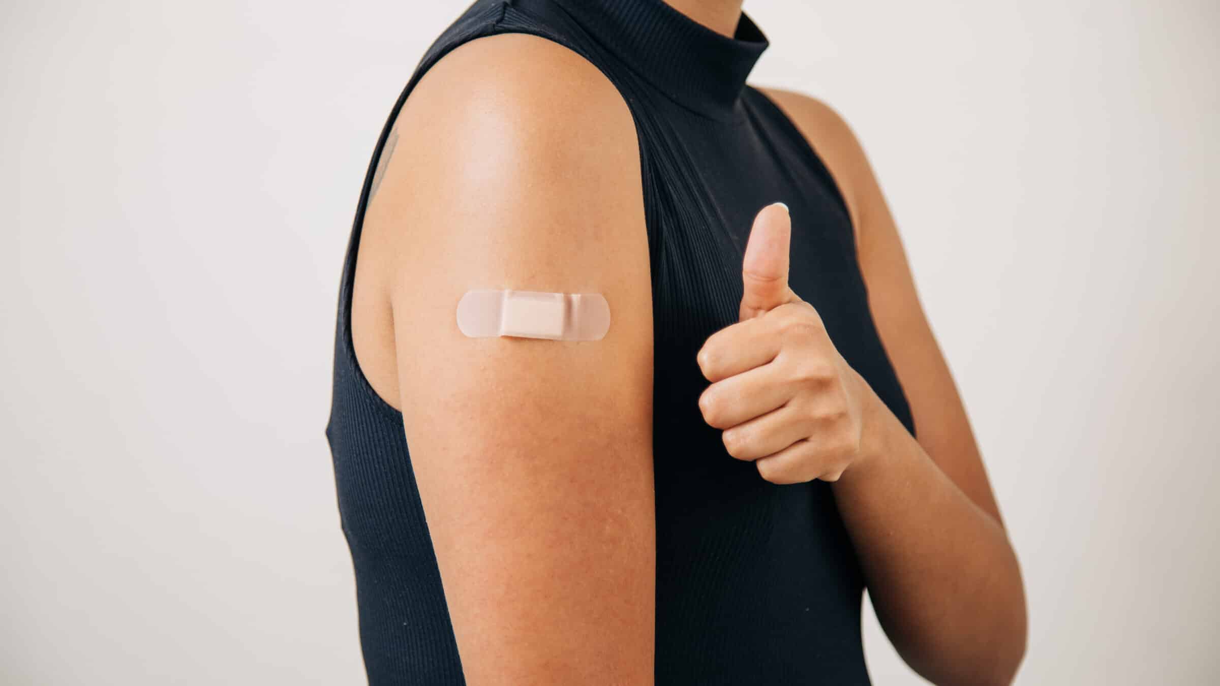 woman vaccinated and with a band-aid on her arm, giving a sign that all is well.