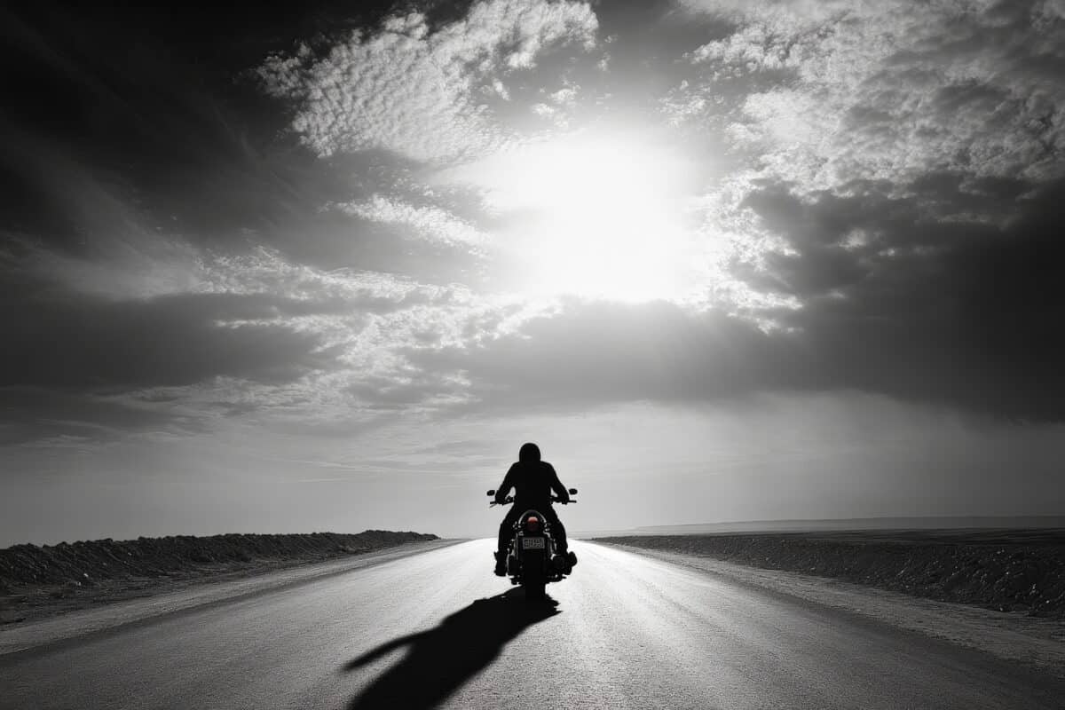 Lone motorcyclist riding on an open road in a black and white landscape
