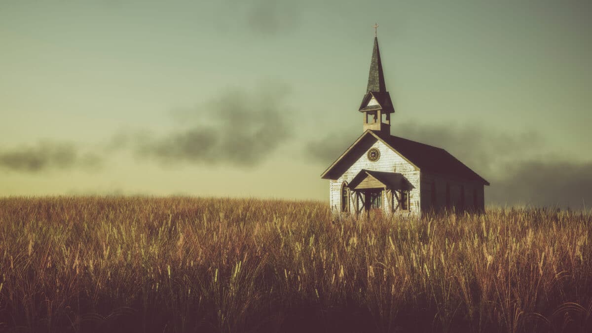 Old abandoned white wooden chapel on prairie at sunset with clou