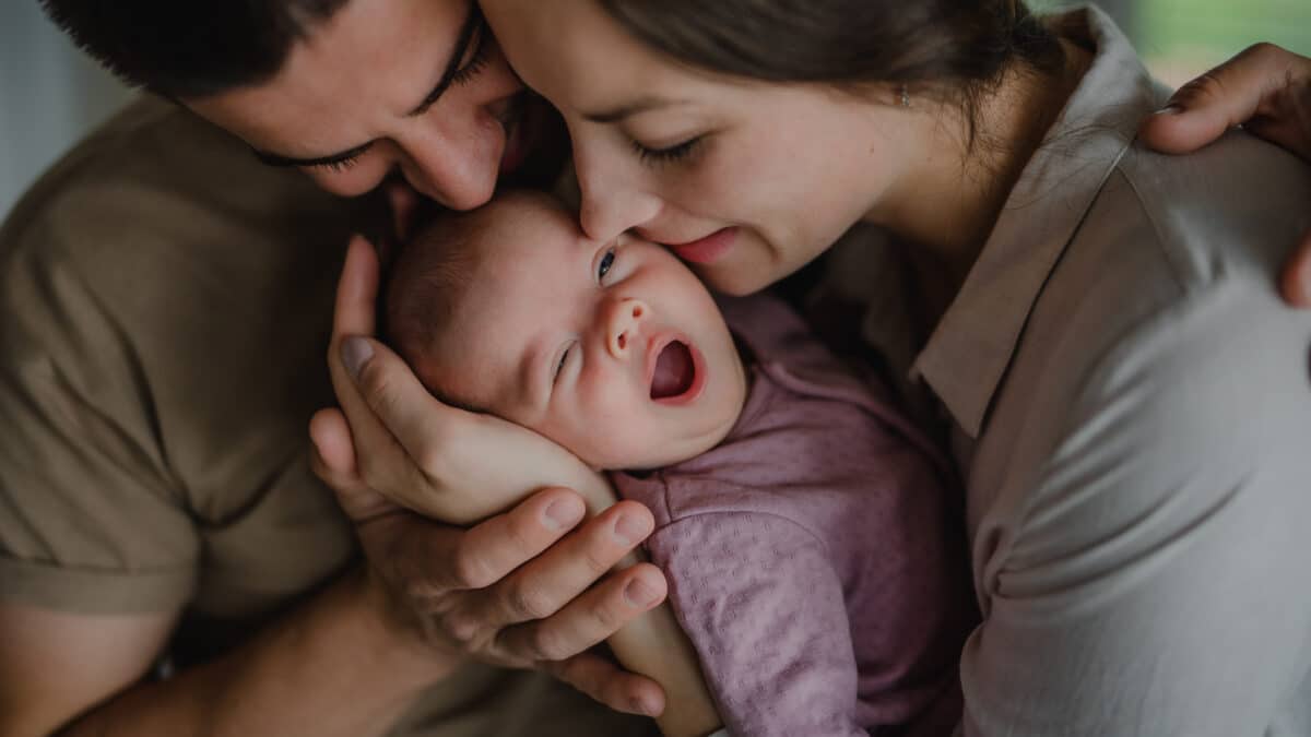 Close up of young parents holding and kissing their newborn baby indoors at home