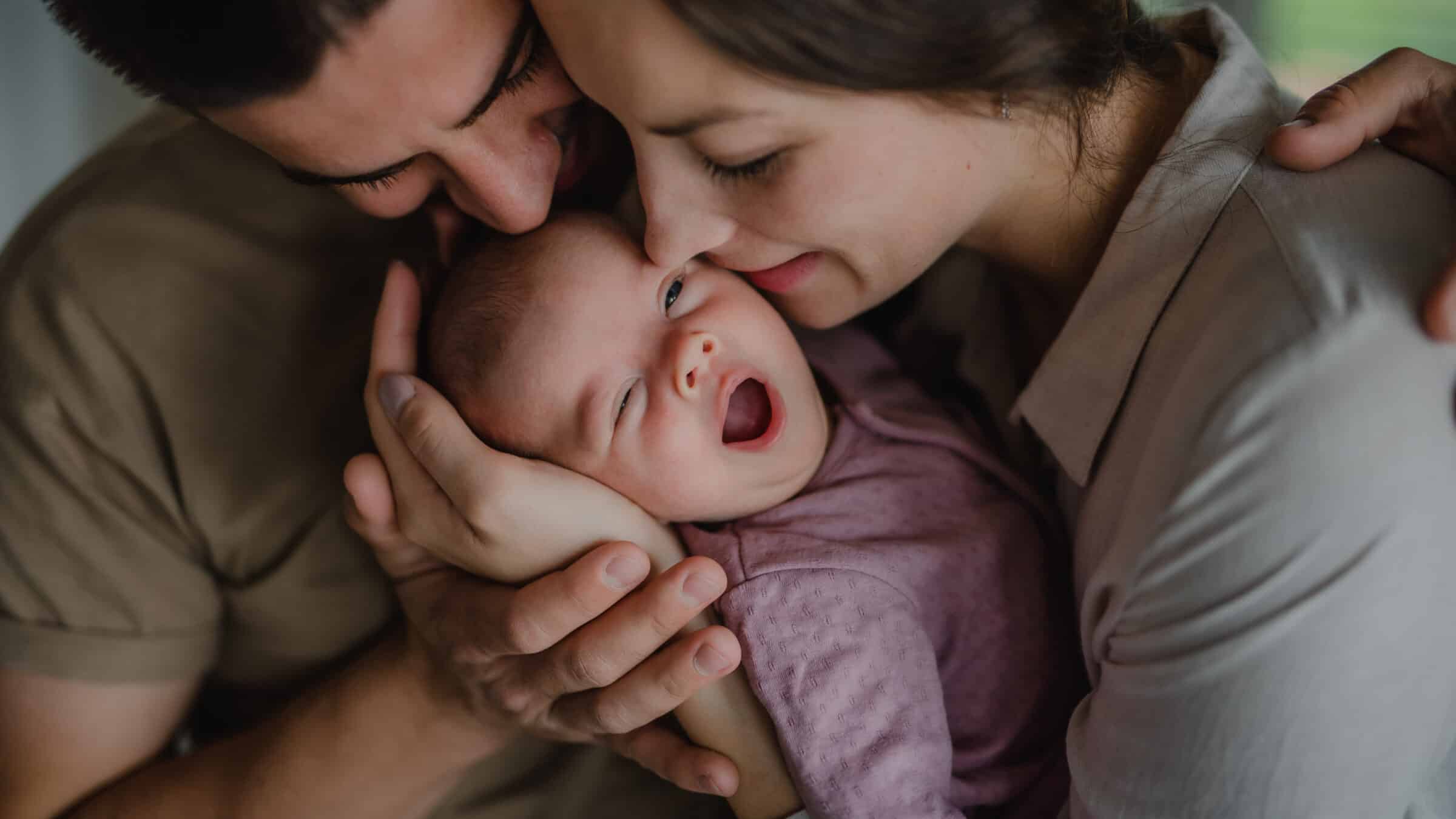 Close up of young parents holding and kissing their newborn baby indoors at home